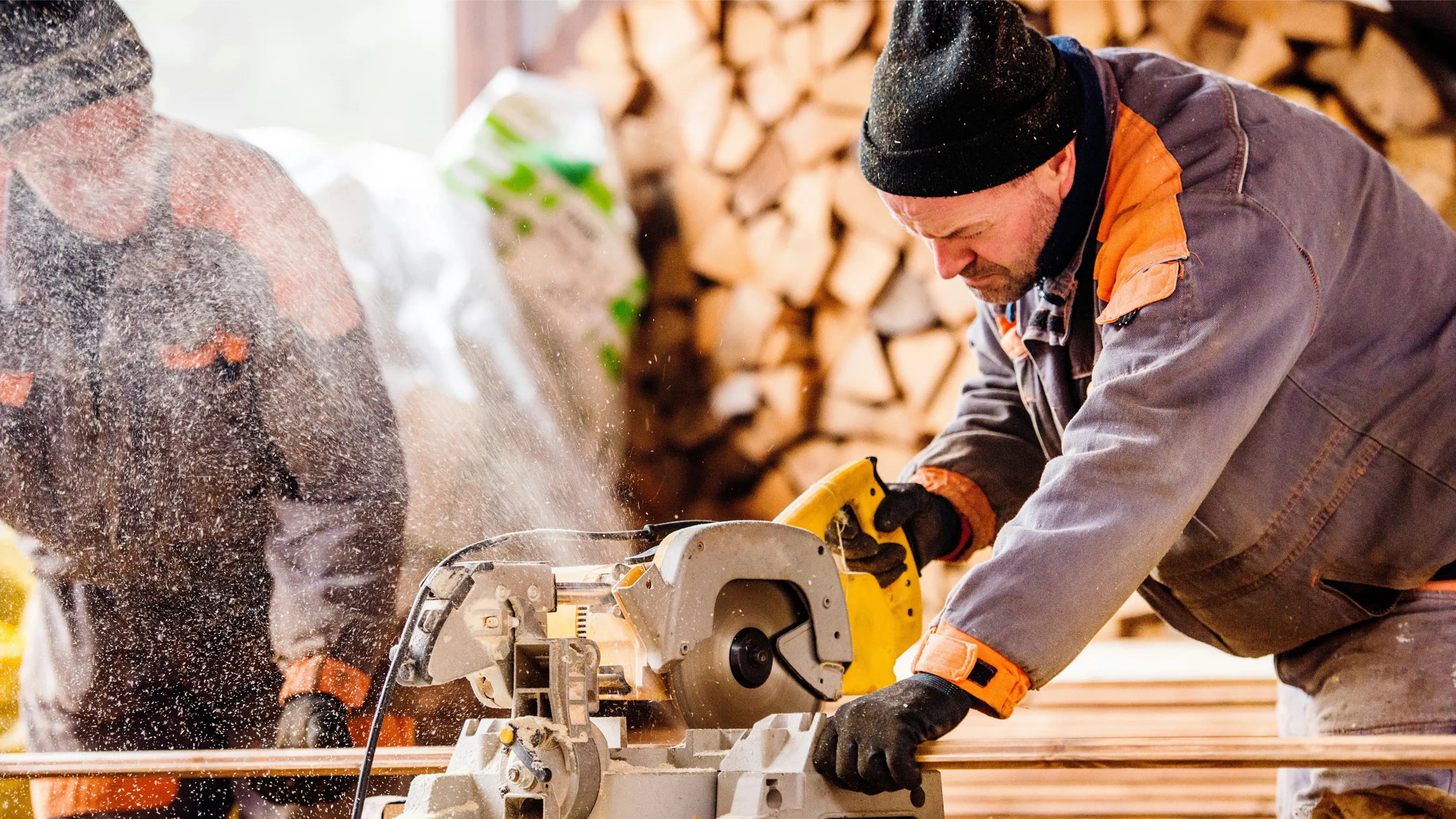 Carpenter cutting lumber with a miter saw in a workshop.