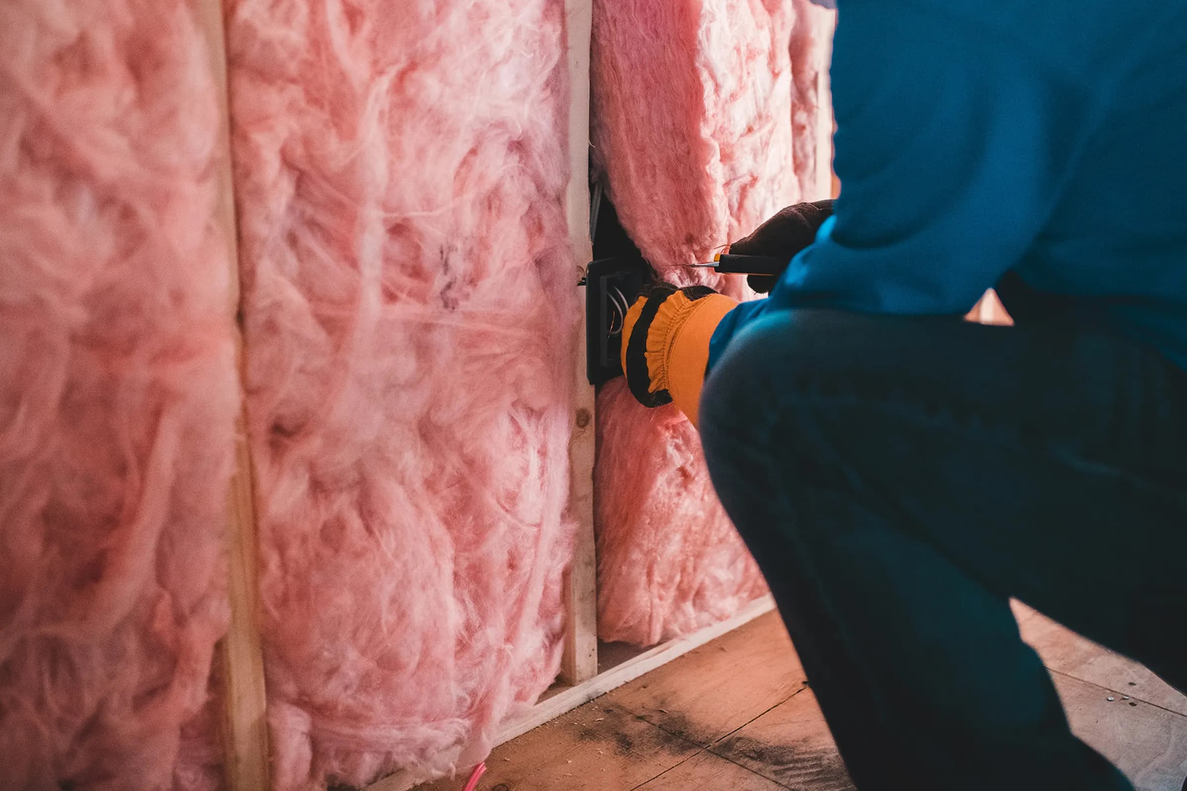 Insulation technician working on a wall in a residential home with pink fiberglass insulation